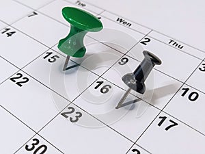 Green and black pushpins stuck into calendar, event reminder