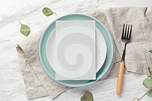 Green blank menu card mockup on plate with fork on linen napkin on marble table