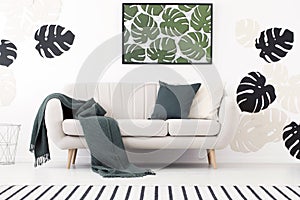 Green blanket and cushion on settee in white living room interior with poster of leaves. Real photo