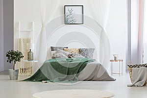 Green blanket thrown on double bed with many pillows and grey sh