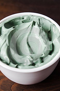 Green (blue) bentonite clay facial mask in a small white bowl. Homemade natural beauty treatment and spa recipe.