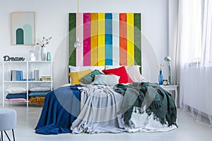 Green and blue blankets on a white bed with rainbow bedhead in white, scandi bedroom interior. Real photo