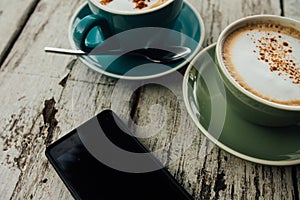 Green and blue cup coffee and smartphone rests on a wooden table