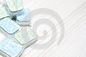 Green and blue dishwasher tablets in water-soluble packaging close up on the table with copy space