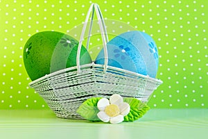 Green and blue Easter eggs in a basket with white flower