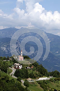 Green and blue mountain landscape with a small red church in Guardia, Trentino, Italy photo