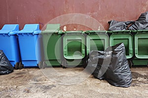 Green and blue plastic recycle bins and black garbage bags on r