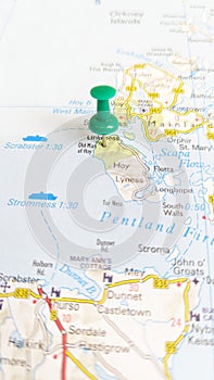 A green board pin stuck in the island of Hoy on a map of Scotland portrait