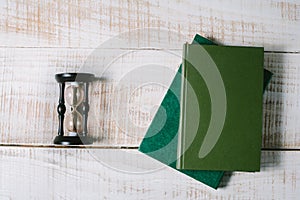 Green books and hourglasses lie on a wooden table. top view