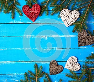 green branches of needles and decorative wicker hearts on a blue wooden background