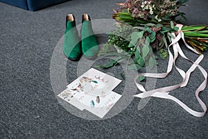 Green bridal shoes, rich green wedding bouquet with pink ribbons and a wedding complimentary lying on a grey floor