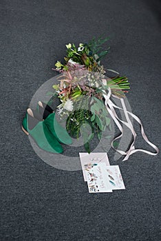 Green bridal shoes, rich green wedding bouquet with pink ribbons and a wedding complimentary lying on a grey floor