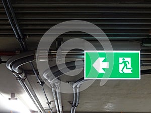 Green bright emergency fire exit with arrow show direction against metal electric wire pipe