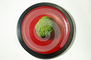 Green Brocolli on Red and Black Plate on White Background