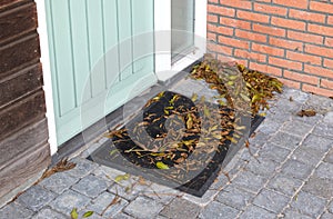 Green and brown autumn leaves piling up in front of the doorstep of a door