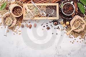 Green and brown decaf unroasted and dark roasted coffee beans in wooden box with scoops setup on white concrete background