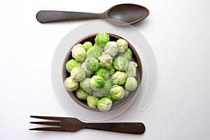 Green Brussels sprouts, its leaves lie on the table and in a wooden bowl, next to a wooden fork and spoon