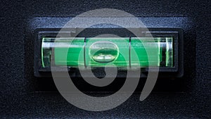 Green bubble level in a horizontal balance position against a black metal background. Macro