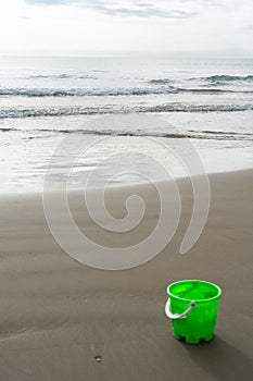 Green bucket on the beach sand