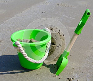 Green bucket and spade on sandy beach