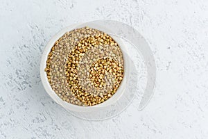 Green buckwheat in white bowl on white background. Dried cereals in cup, vegan food, fodmap diet. Top view, close up