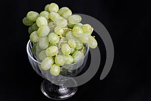 Green bunch of large grapes in a glass cup on a black background photo