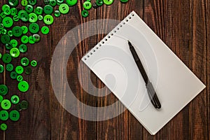 Green buttons of various sizes are scattered in the corner of the wooden background, a notebook and a pen lie. Flatlay