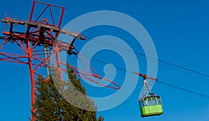 Green cable car speeding upwards. Some fir trees seen lower left