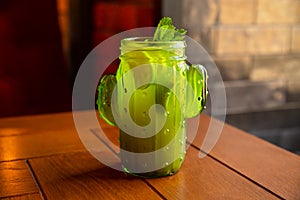 Green cactus shaped glass with Lemonade, lime and mint leaf. Cold green tea or cocktail on wood table. Front view, closeup,