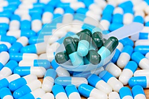 Green capsules in pill spoon on many white blue capsules