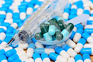 Green capsules in pill spoon with syringe and thermometer on man