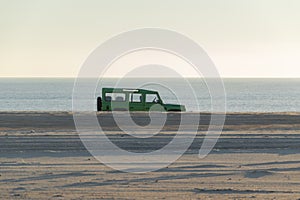 Green car on the beach with the sea in the background and clear sky photo