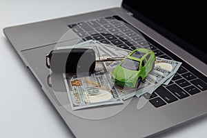 Green car and keys with dollar banknotes and shopping cart on keyboard. Online purchase car concept