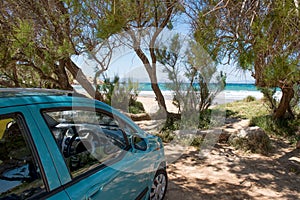 Green car parked on sand beach under the trees