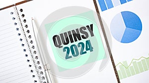 Green card on the white notepad. Text QUINSY 2024. Business concept