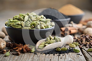 Green cardamom pods in black ceramic bowl in the foreground. Ingredients for cooking. Ayurveda treatments