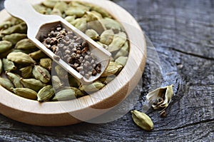 Green cardamom pods and seeds on a wooden plate on vintage wooden background.Elettaria cardamomum.
