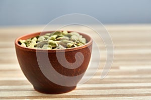 Green cardamon in ceramic bowl on wooden table close-up, top view, selective focus.