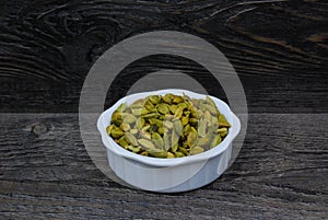 Green Cardamon seeds in a white dish on a rustic background