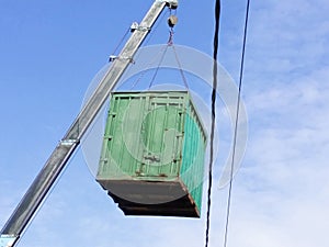 Green cargo container which gray boom with blue hook of truck manipulator lift up near the power line