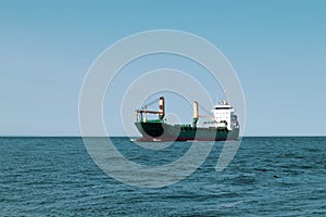 A green cargo ship is sailing at sea