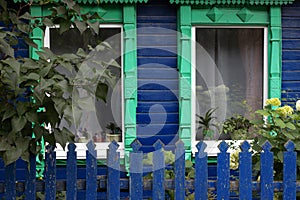 Green carved platband windows with curtains of old traditional russian painted blue wooden house