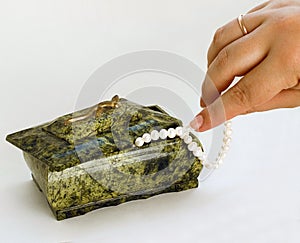 Green Casket hand taking pearl necklace from it