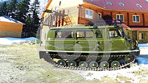 Green caterpillar all-terrain vehicle against the backdrop of chalets and firs in the mountains