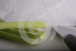 Green Celery Being Sliced on White Cutting Board