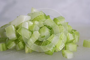 Green Celery Being Sliced on White Cutting Board