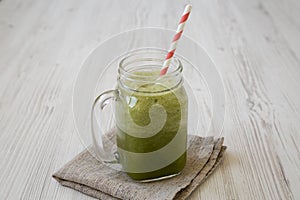 Green celery smoothie in a glass jar over white wooden background, side view