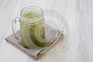 Green celery smoothie in glass jar over white wooden background, side view. Copy space