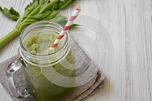 Green celery smoothie in glass jar over white wooden background, side view. Space for text