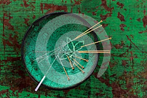 Green ceramic Asian Bowl with needles for acupuncture on an old green paint wooden background